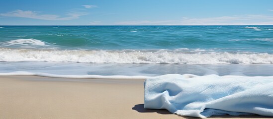 Poster - Serene beach scene with soft turquoise waves gently lapping against golden sand, featuring a crumpled light blue blanket placed in the foreground.