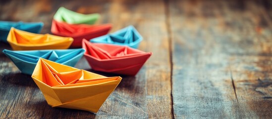 Poster - Colorful origami boats in vibrant yellow, orange, red, and green arranged on a rustic wooden table with a blurred background.