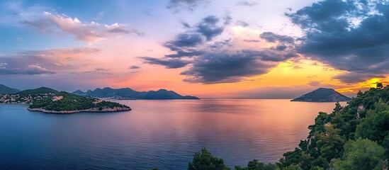 Poster - Lush green hills frame a serene sea under a vibrant sunset sky with pink and orange clouds reflecting in the calm water creating a tranquil atmosphere