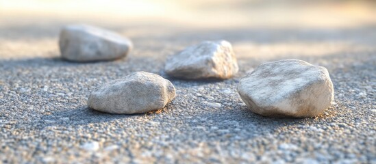 Leinwandbilder - Scattered grey stones arranged on a textured asphalt surface with a blurred background of warm colors and soft lighting.