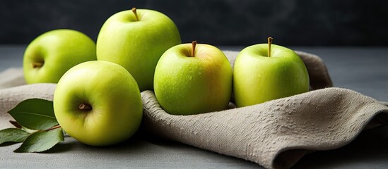 Poster - Fresh green apples arranged elegantly on a soft gray cloth with green leaves, set against a dark textured background, creating a vibrant contrast.
