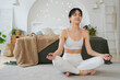 © Юлия Завалишина - Yoga mindfulness meditation. Young healthy woman practicing yoga in living room at home. Woman sitting in lotus pose meditating smiling relaxing indoor. Girl doing breathing practice. Yoga at home