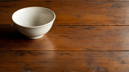 Leinwandbilder - A small white ceramic bowl rests centrally on a weathered wooden table, bathed in soft natural light, creating a serene and simple atmosphere