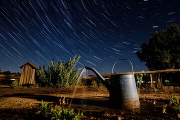 Watering cans pouring starlit skies, night photography with star trails