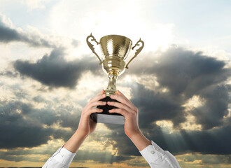Wall Mural - man holding golden trophy against sky, closeup