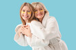 © Pixel-Shot - Happy young woman and her mother in bathrobes with under-eye patches on blue background