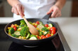 © He - woman in an apron cooking vegetables in a pan on a stove