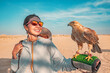 © EdNurg - Smiling tourist holding a falcon on her arm while enjoying the sunny desert landscape of the United Arab Emirates, experiencing local culture