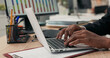 © ABCreative - Close-up of silver latop standing on wooden desk, dark-skinned man working on it, young hands, typing text into keyboard, tapping fingers on computer