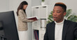 © ABCreative - dark-skinned office worker sits in front of computer at desk having video conversation internet connection via webcam discussing company matters with co-workers explaining completed chart project