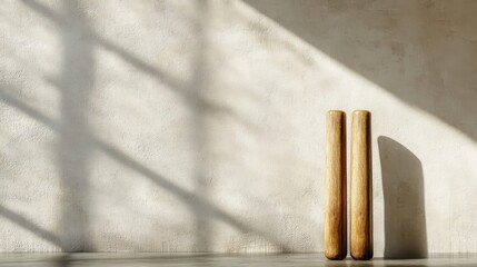 Poster - Two wooden cylindrical objects stand against textured wall with shadows