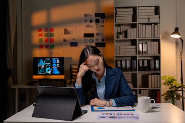 Fototapete - Stressed Asian businesswoman having headache working late at night in office