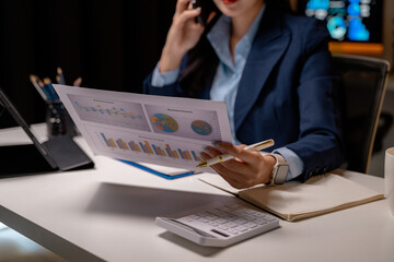 Fototapete - Businesswoman analyzing financial charts and speaking on the phone at night
