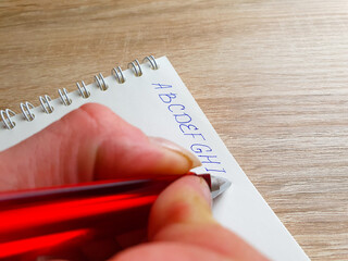 Fototapete - Girl writes the English alphabet on a notebook with a pen. The letters of the English alphabet, learning English.