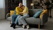 © kinomaster - Happy couple celebrating valentines day at home, man and woman sitting on the sofa, cuddling and hugging, happy expression.