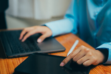 Poster - Close-Up View of Hands Using Laptop and Tablet on Wooden Table in Modern Workspace, Business concept.