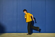 © Elena - Student walks playfully along a bright blue wall while smiling and enjoying the moment in an urban setting