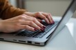 © SimpleDesignStudio - A Close-Up of a Woman's Hands Typing on a Laptop Keyboard in a Cozy Workspace Featuring a Brown Sweater and Elegant Nail Polish