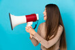 © luismolinero - Young caucasian woman isolated on blue background shouting through a megaphone to announce something in lateral position