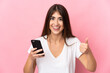 © luismolinero - Young caucasian woman isolated on pink background using mobile phone while doing thumbs up