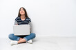 © luismolinero - Young caucasian woman with a laptop sitting on the floor isolated on white background looking up while smiling