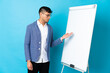 © luismolinero - Young Colombian man isolated on blue background giving a presentation on white board