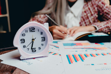 Poster - Close-Up of Alarm Clock on Desk with Business Charts and Woman Writing Notes, Business concept