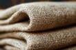 © marimalina - Textured burlap fabric folded neatly on a wooden surface under natural light showcasing its earthy tones and rustic aesthetic