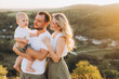 © anatoliycherkas - Happy Family Enjoying a Scenic Sunset View in the Countryside with Smiling Parents and Baby