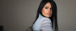 © Chari - Woman with long dark hair seated in a neutral-toned room looking back thoughtfully
