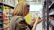 © Alexander - Woman carefully examines the label of a jar of food while shopping in a brightly lit supermarket, demonstrating consumer awareness and decision making