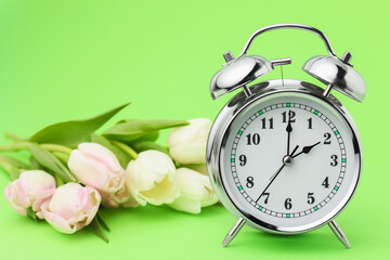 Poster - Spring time. Alarm clock and beautiful tulips on green background, closeup
