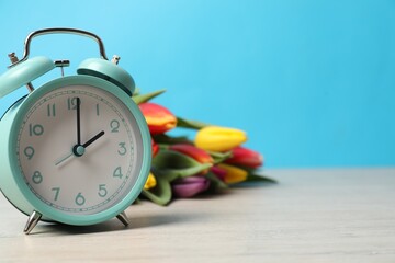 Poster - Spring time. Alarm clock and beautiful tulips on wooden table against light blue background, space for text