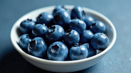 Poster - A close-up of plump, juicy blueberries in a pristine white bowl, glistening with moisture on a deep blue background.