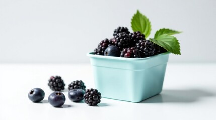 Poster - A delightful arrangement of plump blackberries and blueberries, nestled in a pastel blue container, garnished with vibrant green leaves, sits on a pristine white surface.