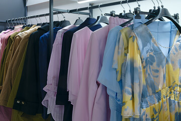 Poster - A rack of clothes with a blue shirt on the top shelf. The clothes are hanging on hangers and are organized by color