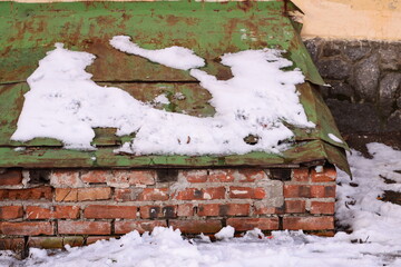 Poster - A green roof covered in snow next to a brick wall, ideal for winter scenes or seasonal decorations.