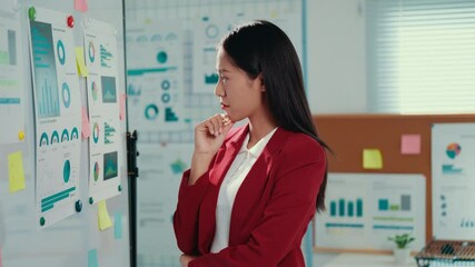 Aufkleber - Experienced businesswoman wearing red suit analyzing marketing data, developing strategic insights while taking detailed notes in contemporary corporate workspace