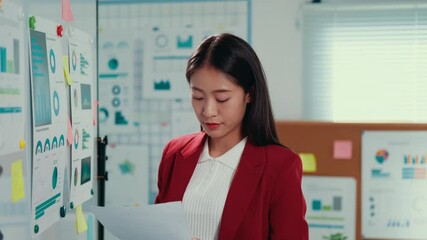 Aufkleber - Professional Asian businesswoman reviewing financial data, pointing at whiteboard charts, holding corporate documents in contemporary workplace setting