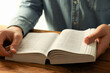 © New Africa - Man reading Holy Bible in English language at wooden table, closeup
