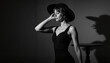 © ChrisKuz - Elegant woman posing in black dress and wide-brim hat, vintage noir