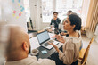 © Maskot - High angle view of businesswoman explaining creative strategy while sitting with laptop at meeting room in office