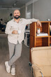 © Maskot - Portrait of smiling male entrepreneur holding coffee cup while leaning on shelf with legs crossed at ankle in creative o