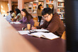 © Maskot - Young male university student writing assignment in book while sitting at library desk