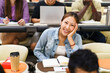 © Maskot - High angle portrait of smiling female student sitting at desk in lecture hall