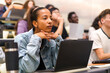 © Maskot - Young female student with hands on chin sitting at desk in lecture hall