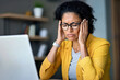 © vejaa - Black mature woman suffering from headache stress while using computer at home office. Upset tired middle aged woman holding with hands head feeling bad and overwork