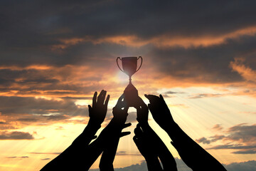 Wall Mural - silhouettes of people reaching for trophy against sunset sky, closeup