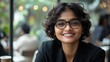 © nabila - Smiling woman with curly hair and glasses in a modern cafe setting