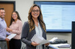 © top  success - Professional woman smiling while holding documents in an office with colleagues in the background